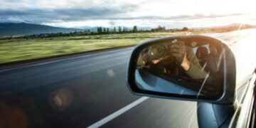 photographing from car window. Reflection in car mirror of hands with camera.